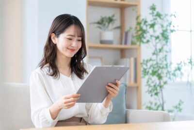 スマートフォンと書類を手に、買取のお申し込み内容を確認している女性